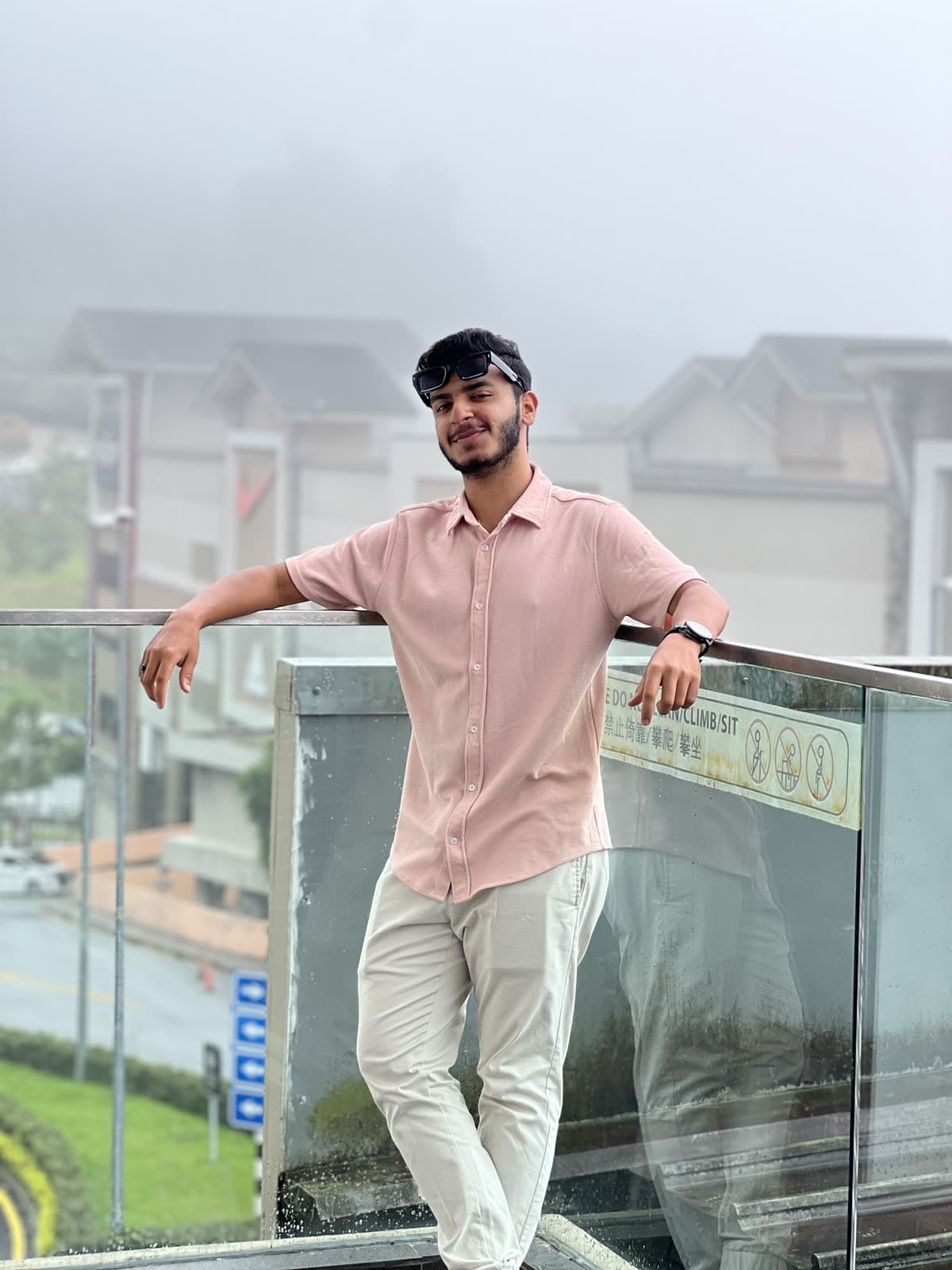 Mazin leaning on a glass balcony rail with the misty Genting hills behind him