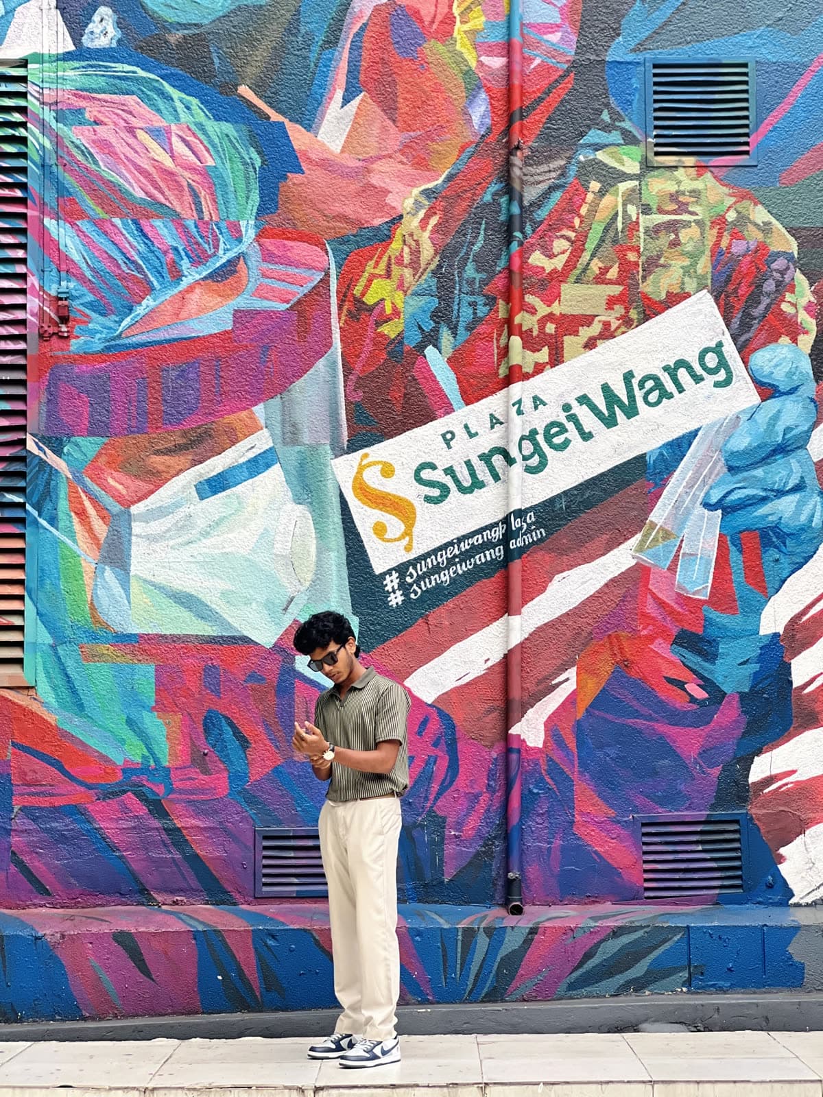 Mazin standing in front of the colorful Sungei Wang mural in Kuala Lumpur
