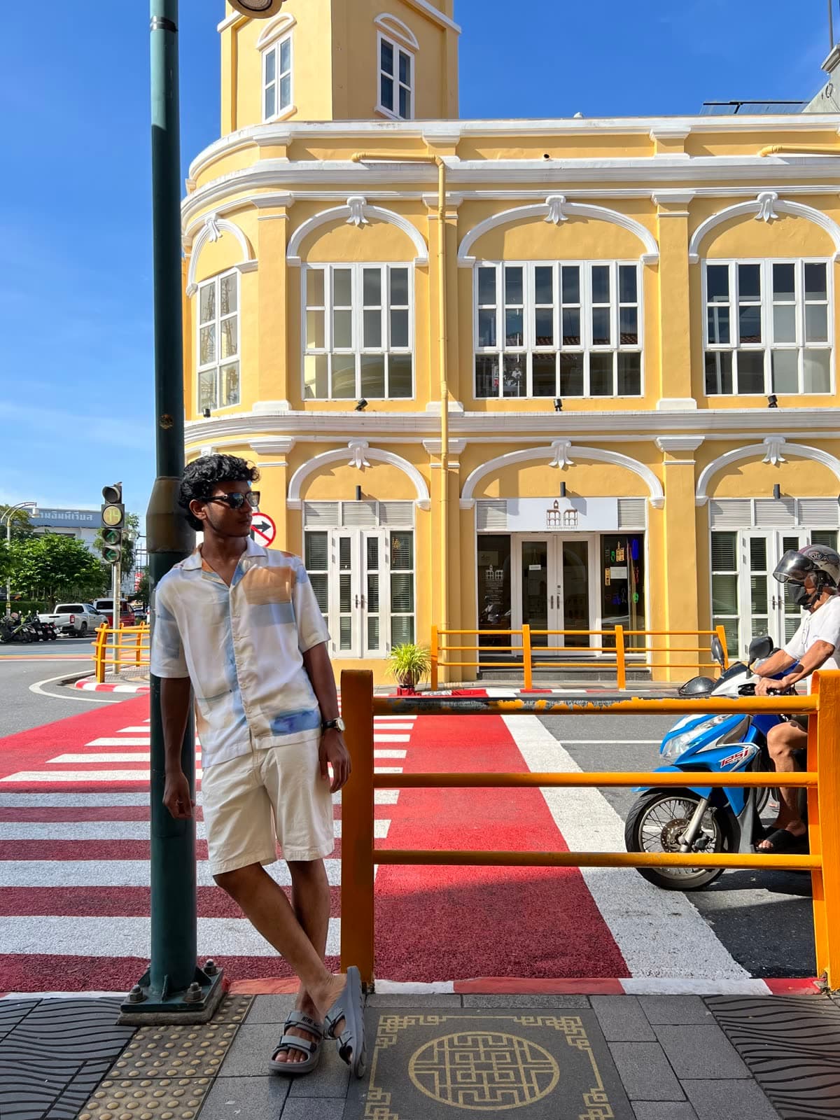 Mazin leaning on a pole in front of a yellow Sino-Portuguese building in Phuket Old Town